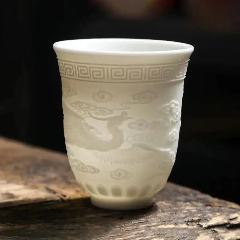 Delicate translucent white jade tea cup set with embossed cloud and dragon designs and greek key pattern near rim