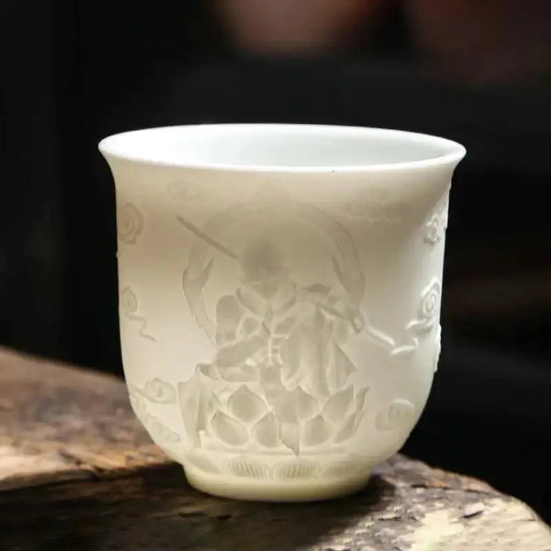 A delicate white porcelain tea cup with carved seated figure and lotus motifs in a hand carved tea cup set