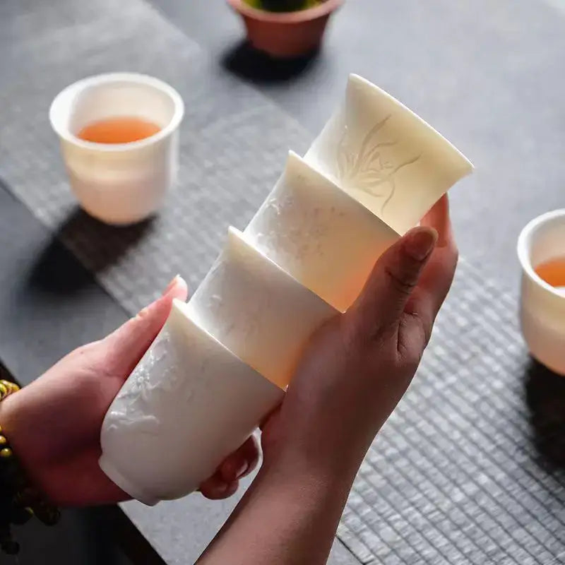 A set of four off-white hand carved translucent white jade ceramic tea cups with engraved floral patterns for dining