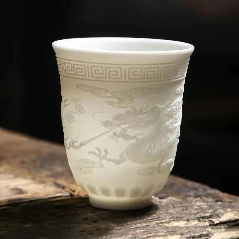 A delicate white porcelain tea cup set with embossed dragon and cloud motifs and a greek key pattern near the rim