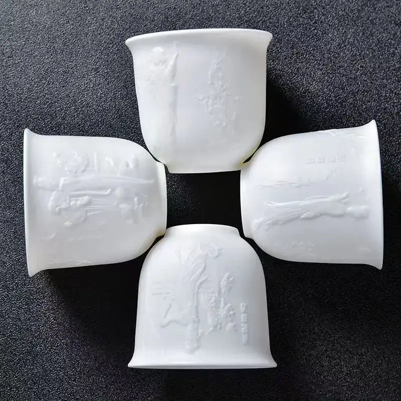 Four white porcelain tea cups with embossed traditional chinese motifs in a hand carved translucent white jade cup set