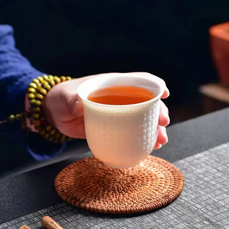 A white ceramic tea cup with geometric pattern and textured body filled with amber tea from a jade cup set