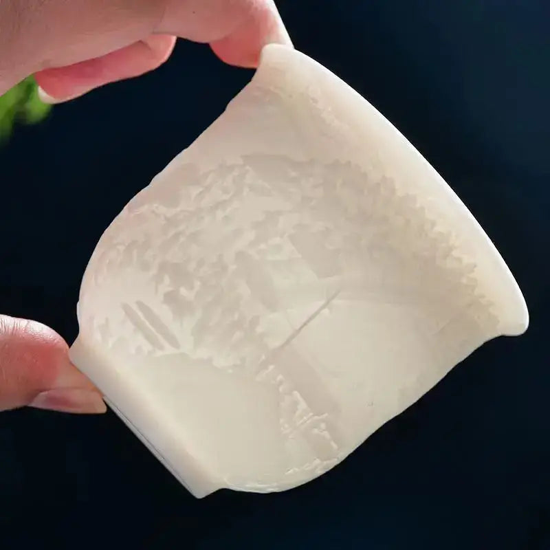 A translucent white ceramic tea cup with a hand carved landscape design in a jade tea cup set for dining room use