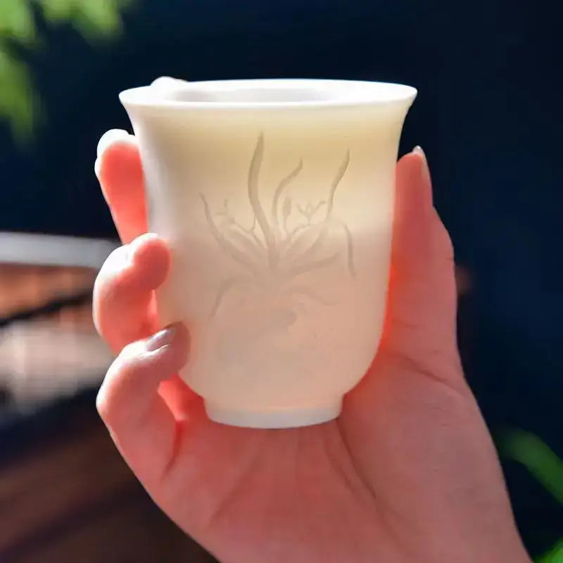 A hand carved translucent white jade tea cup set featuring a delicate etched floral design on a ceramic cup