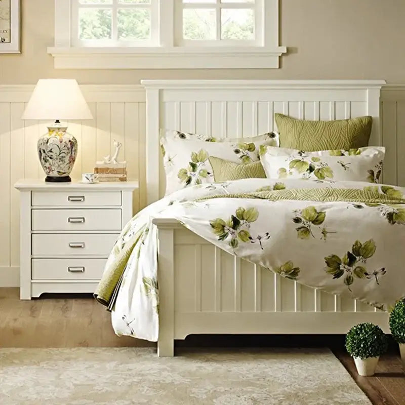 White wooden bed with vertical slats and green leaf bedding beside decorbites coral flower bird ceramic table lamp