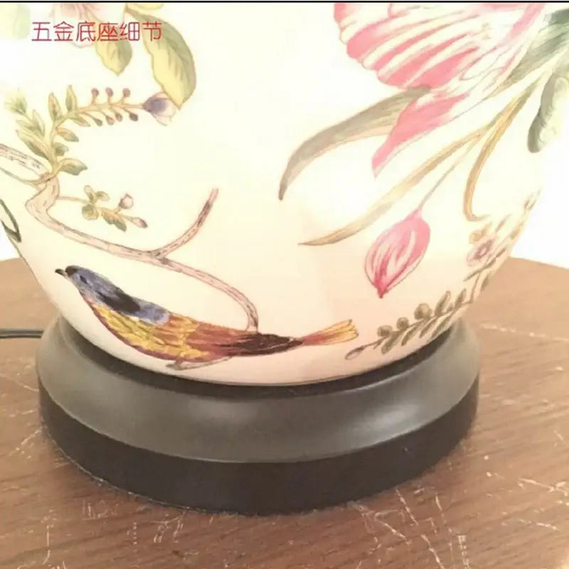 A cream-colored ceramic table lamp with hand-painted coral flower bird motifs on a dark metallic base by decorbites coral flower