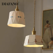 Two cream-colored decorbites ceramic pendant lights with gold-toned fixtures and hand-painted patterns for dining room