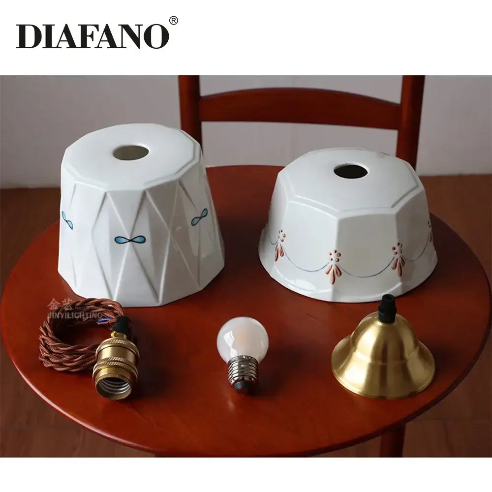 Two white decorbites ceramic pendant light shades with geometric facets and hand painted blue bow and brown floral motifs
