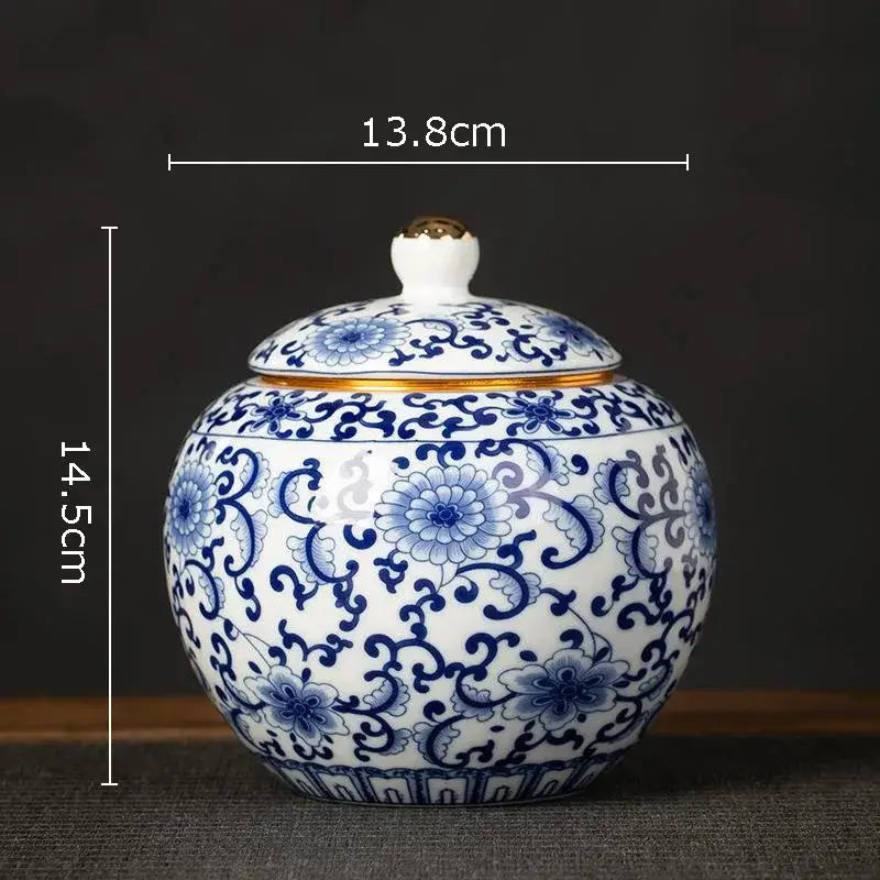 A hand-painted white porcelain tea canister with intricate blue floral patterns and a gold-trimmed lid for kitchen storage