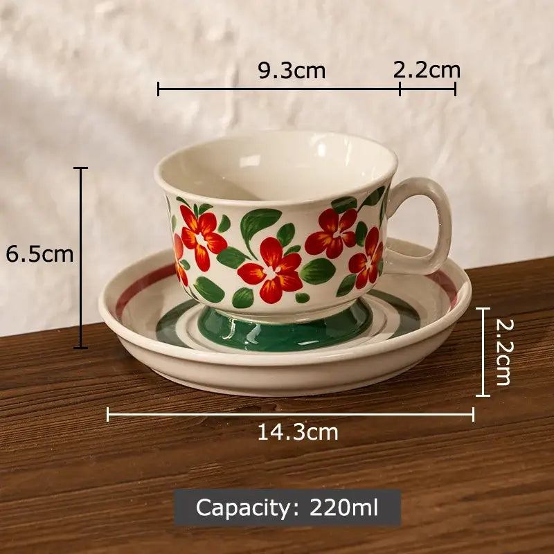 A white ceramic teacup with a handle featuring a decorbites flowers pattern of red flowers and green leaves