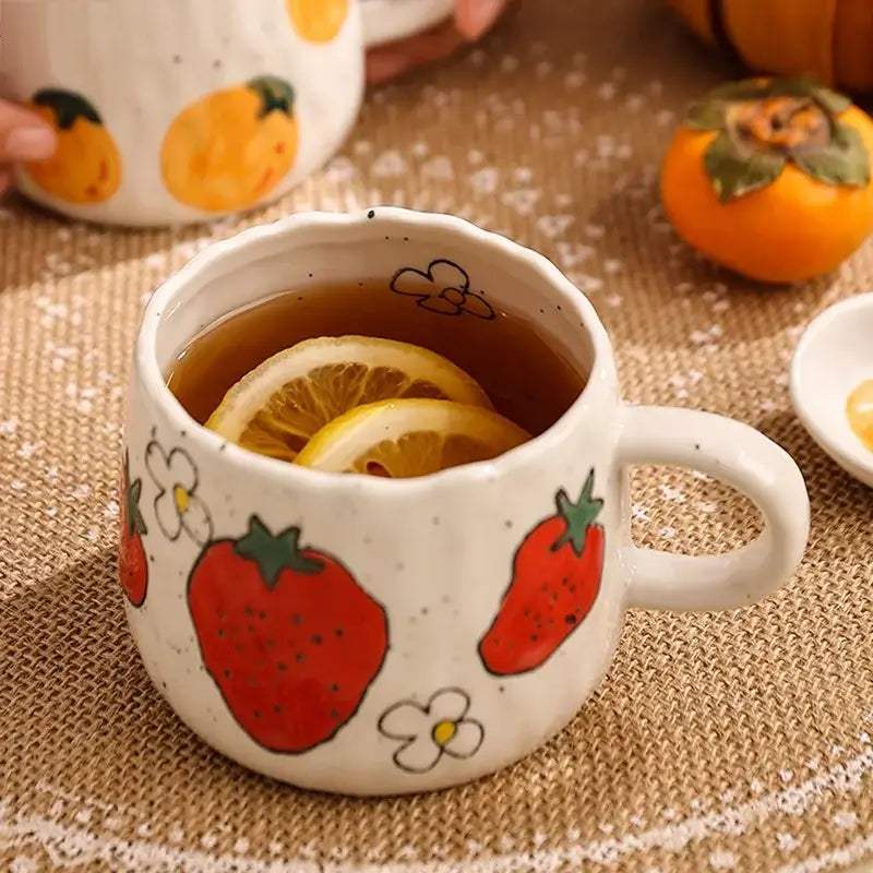 White ceramic cartoon fruit ceramic mug with hand-painted red strawberries and flowers filled with tea and lemon slices