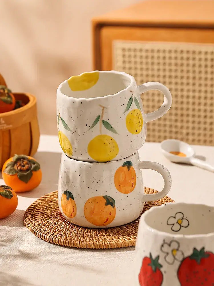 Stacked ceramic mugs with hand-painted yellow and orange cartoon fruit designs on speckled white decorbites ceramic cups