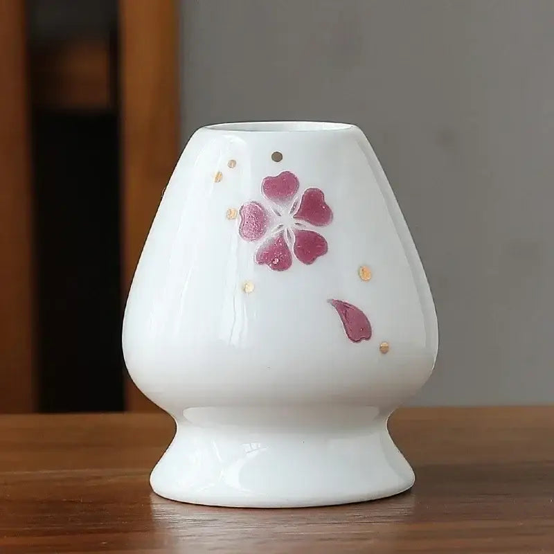 Hand painted white ceramic oil burner with pink cherry blossom and gold dots used as a matcha whisk holder stand