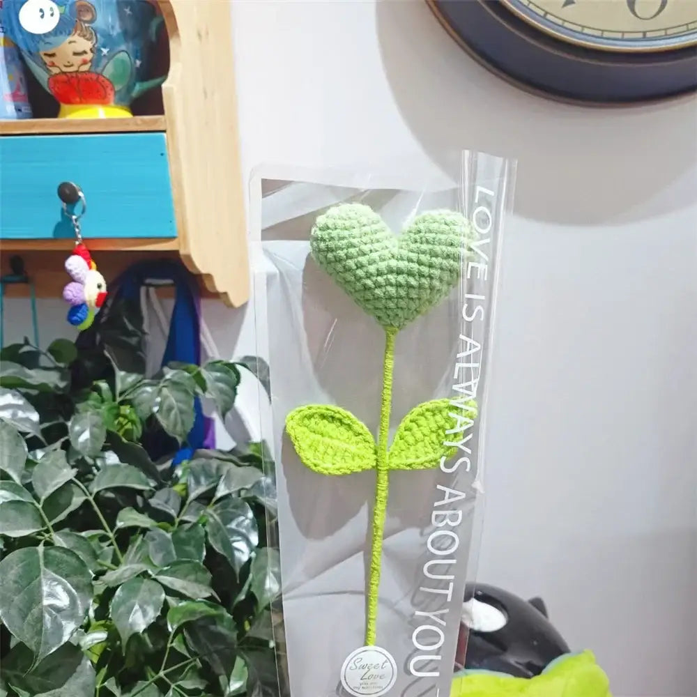 A hand woven love heart yarn crochet flower bouquet with a green heart and lime leaves packaged in clear plastic