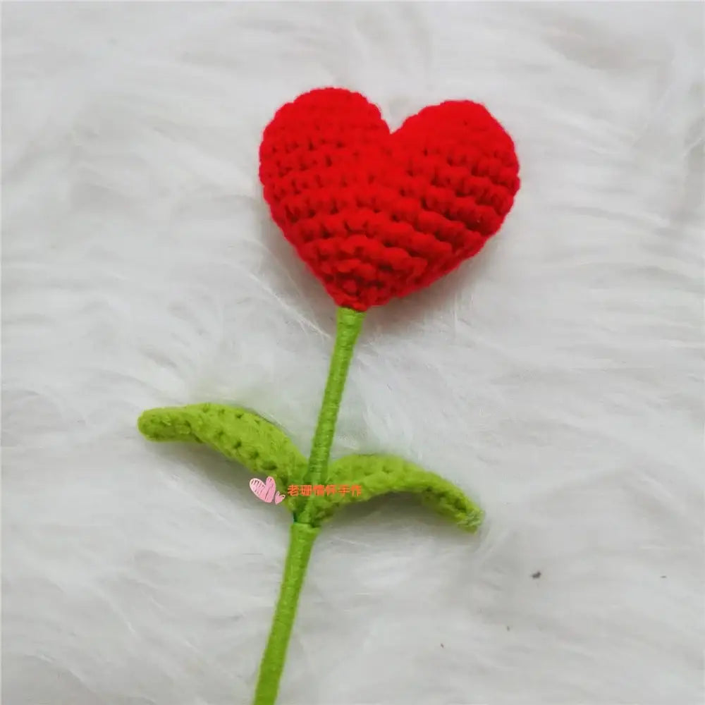 A hand woven love heart yarn crochet flower in red with green stem and leaves for bedroom decor