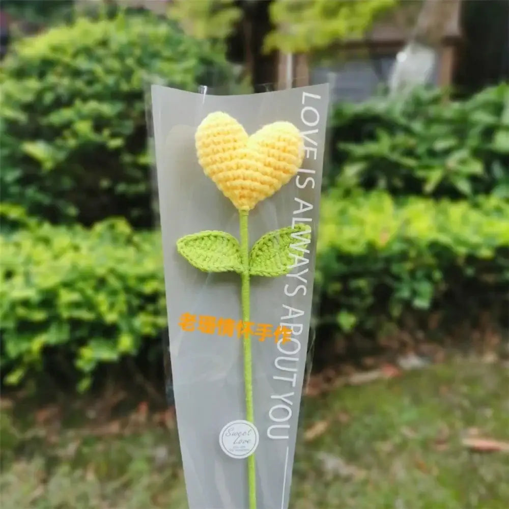 Hand woven love heart yarn crochet flower bouquet with yellow heart shaped bloom and green leaves in clear packaging
