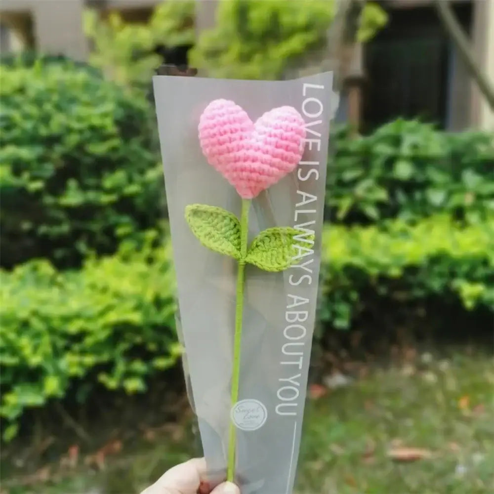 Hand woven love heart yarn crochet pink flower with green leaves in clear plastic sleeve for bedroom decor
