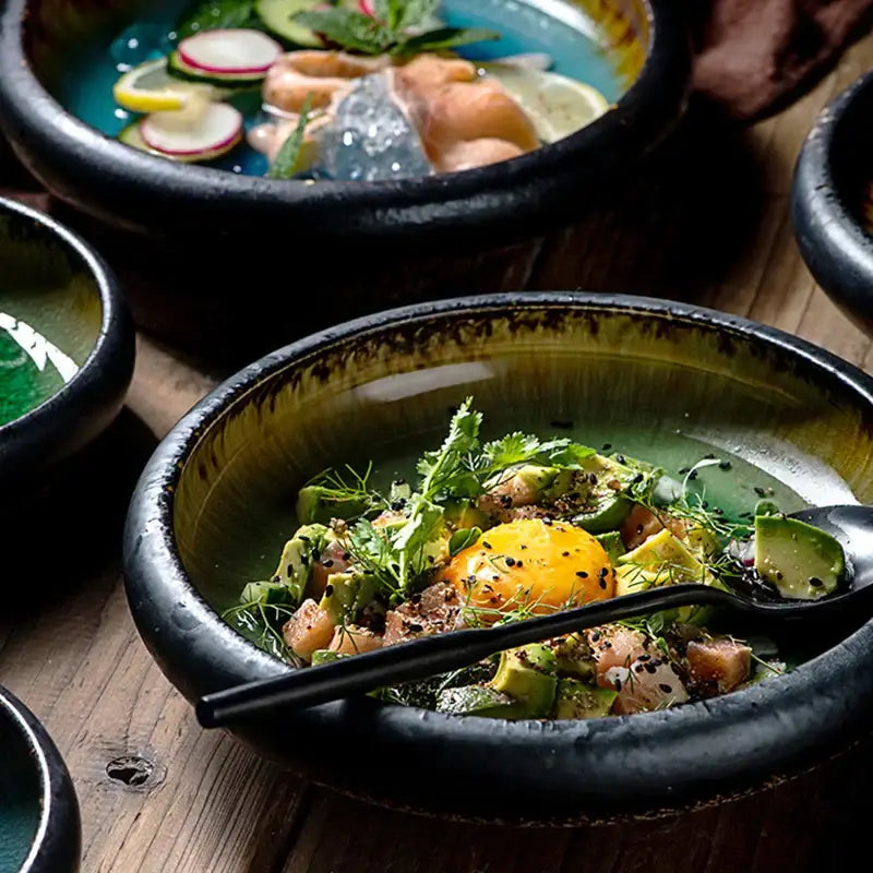 A rustic ceramic sushi plate with a dark rim and olive-green interior holds a vibrant avocado fish salad