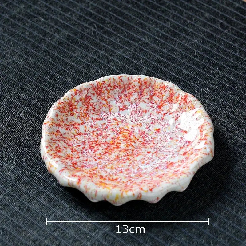 A delicate white ceramic dish with scalloped edge and red orange speckles complementing a hammer pattern ceramic mug set