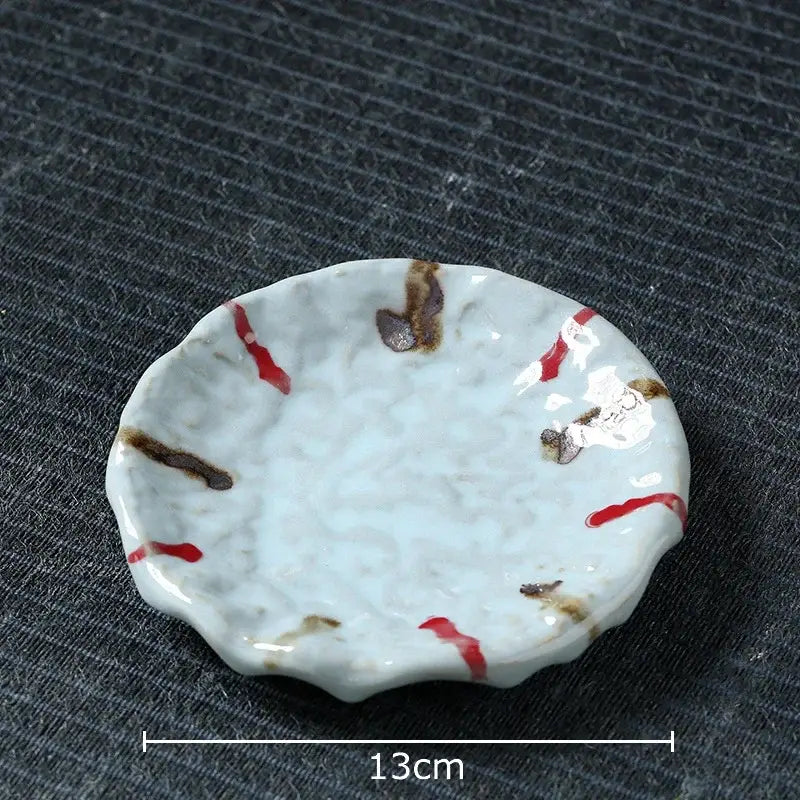 A delicate white ceramic dish with scalloped edge and red brushstroke patterns for hammer pattern ceramic mug set