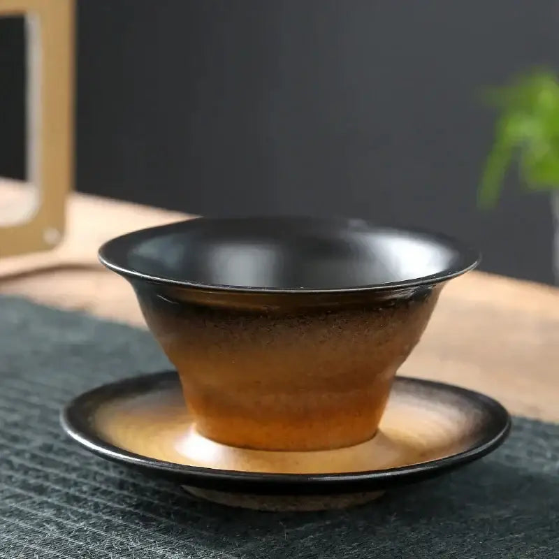 Handcrafted ceramic latte coffee cup with glossy black rim and amber brown gradient glaze on matching saucer