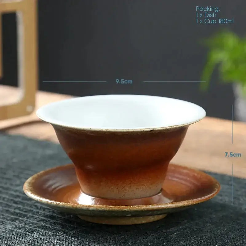 Handcrafted brown and amber ceramic latte coffee cup with white interior resting on matching saucer for dining room use