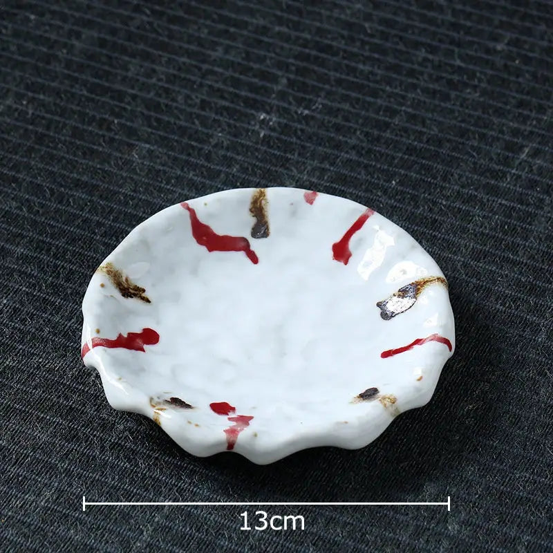 A white ceramic dish with scalloped edge featuring red and brown splatter patterns for hammer pattern porcelain set