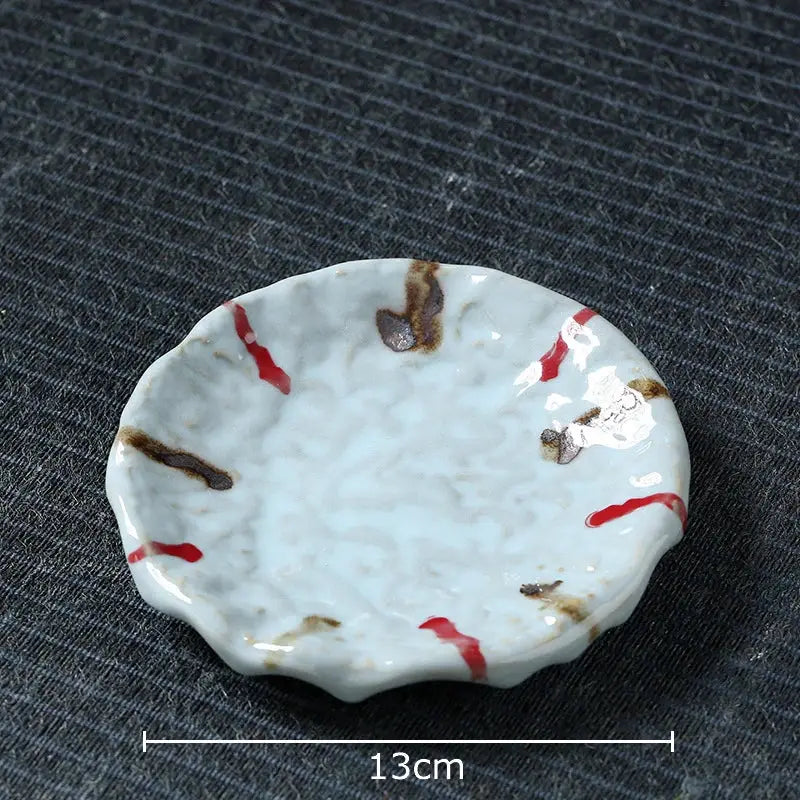 A delicate white ceramic dish with a scalloped edge and irregular red and brown glaze streaks complements hammer pattern porcelain mugs