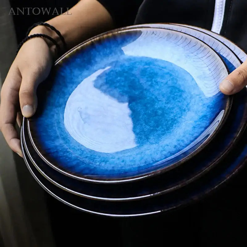 A set of three handcrafted ceramic round plates with gradient blue glaze and subtle crackle texture stacked neatly