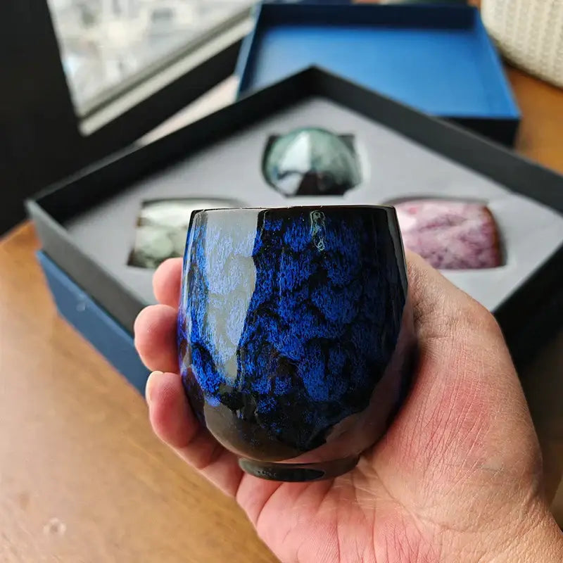 A hand holds a glossy deep blue handcrafted ceramic cup from decorbites ceramic cups set for dining room tea pottery