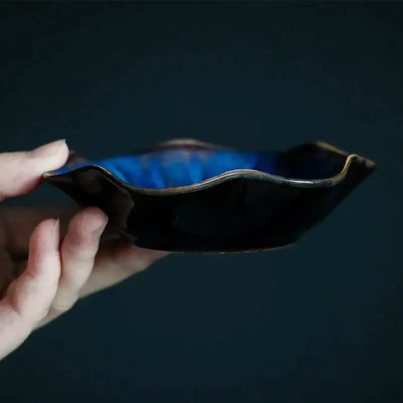 A hand holds a decorbites ceramic japanese style scalloped dipping bowl with glossy black exterior and blue interior