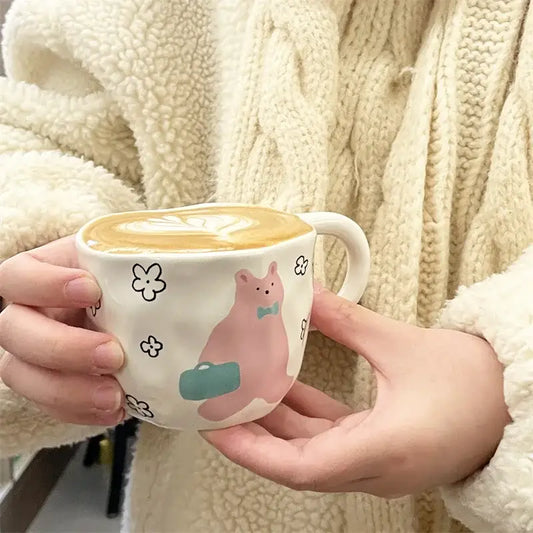 Handcrafted white ceramic bear mug with a pink cartoon bear holding a green suitcase and small black flowers