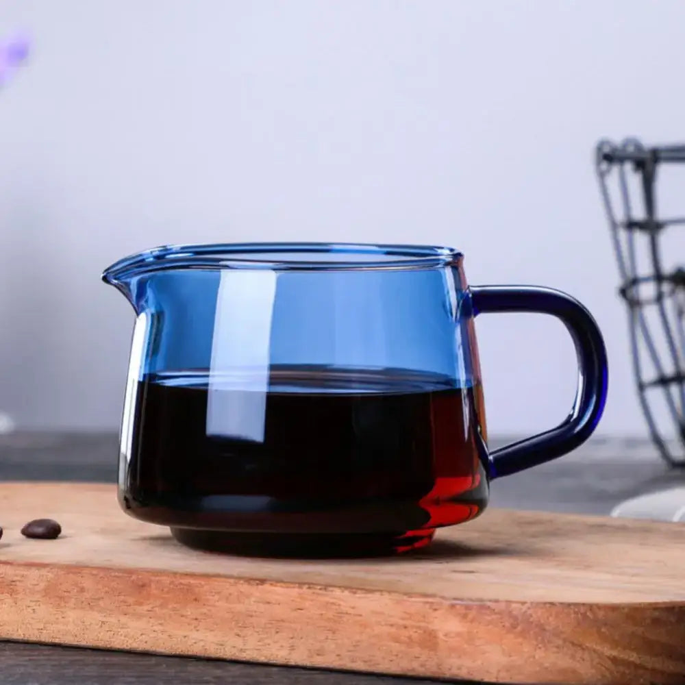 Handmade translucent blue glass coffee sharing pot with dark handle filled with black liquid for kitchen brewing