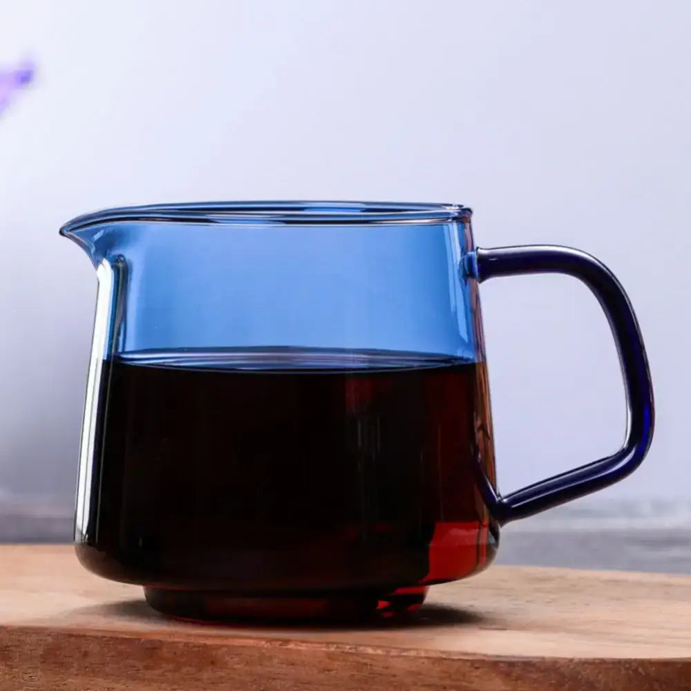 Handmade translucent blue glass coffee sharing pot with dark handle filled with black coffee for kitchen brewing