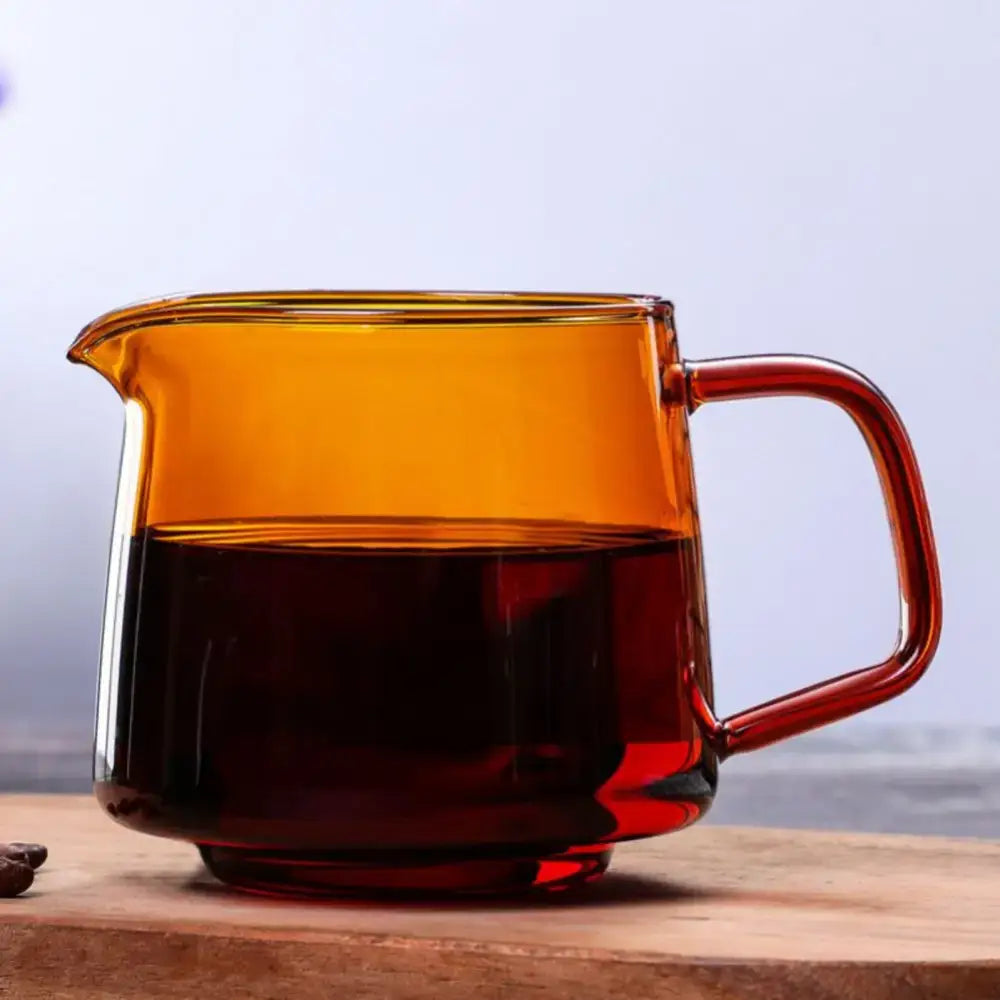 Handmade blue glass coffee sharing pot with amber-tinted glass pitcher half-filled with dark liquid and curved handle