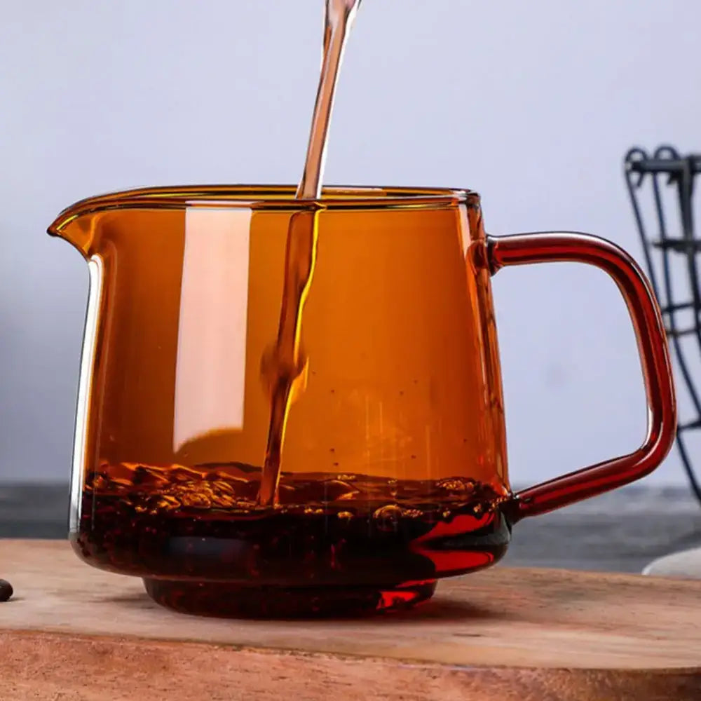 Amber-tinted glass coffee sharing pot with sturdy handle and spout filled with dark liquid for kitchen brewing