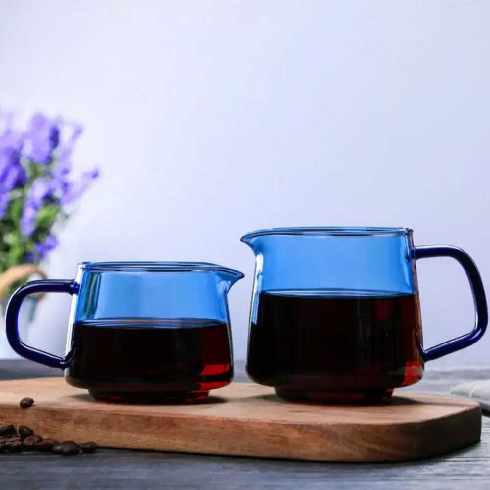 Two translucent blue glass coffee sharing pots with dark handles filled with rich brown liquid for brewing