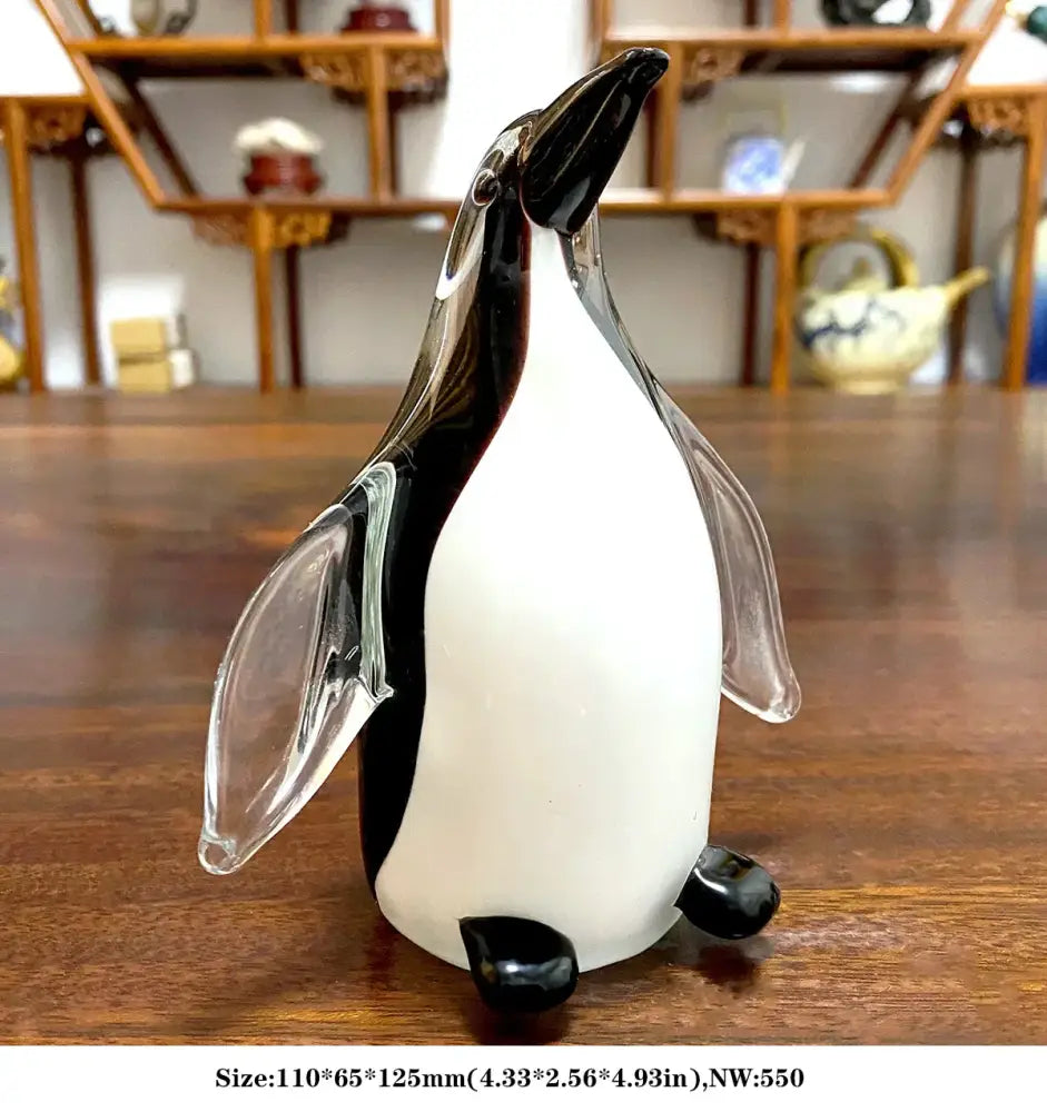 A translucent glass penguin figurine with glossy black head wings and feet contrasting its white body in sika deer decor