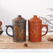 Two ceramic tea mugs with lids in dark gray and terracotta orange featuring golden dragon decorbites dragon purple clay designs