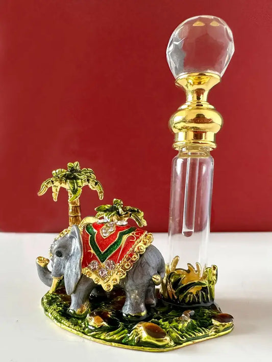 Handmade crystal perfume bottle with golden cap beside a decorative elephant figurine with red and gold blanket