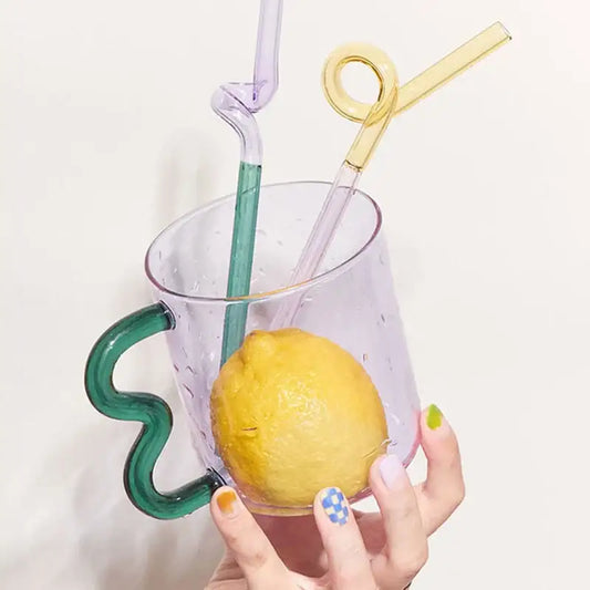 A handmade glass mug lavender with a wavy green handle holds a lemon and colorful straws by decorbites handmade glass