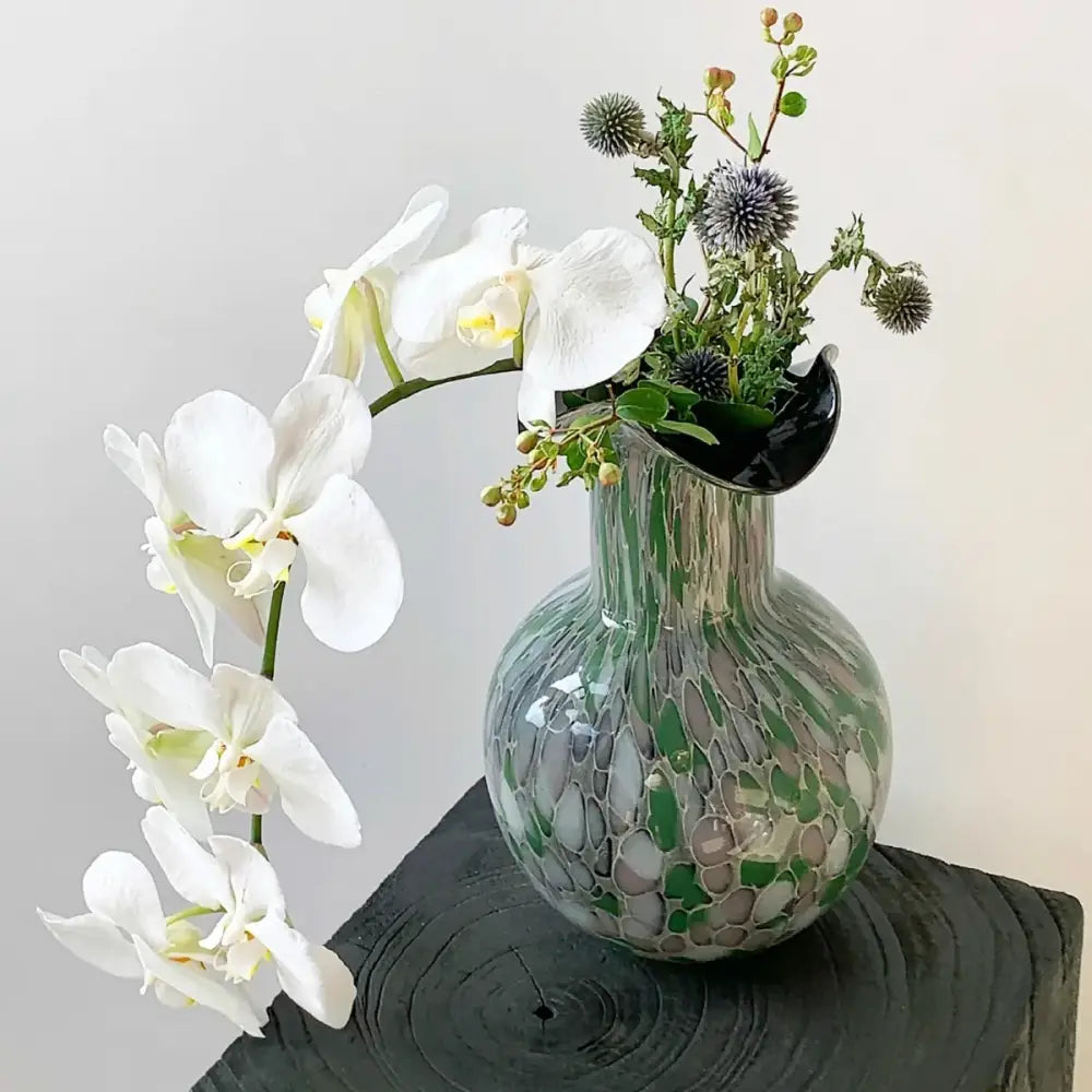 Handmade glass vase pebble with emerald and silver swirling decor holding white orchids and thistle flowers