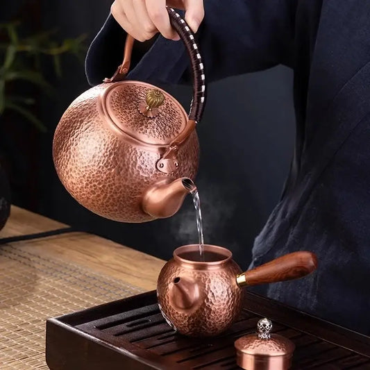 Handmade hammered copper tea pot with knitting handle and floral lid pouring steaming tea into matching copper pot decorbites handmade copper
