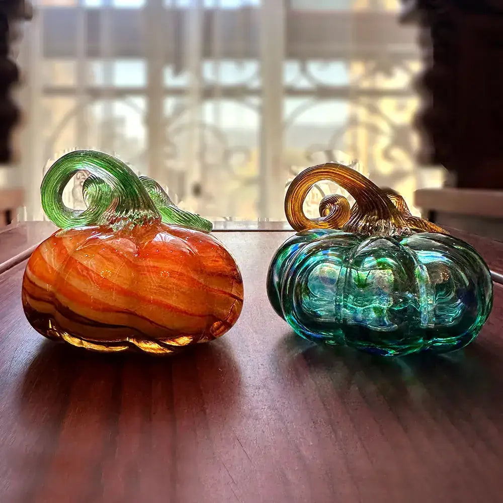 Two handmade glass pumpkin figurines with iridescent teal, green, orange, and amber hues for living room decor