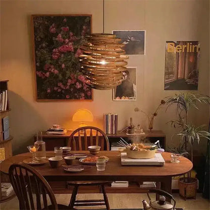 Handmade warm-toned tiered bamboo birdnest pendant light hanging above wooden dining table by decorbites