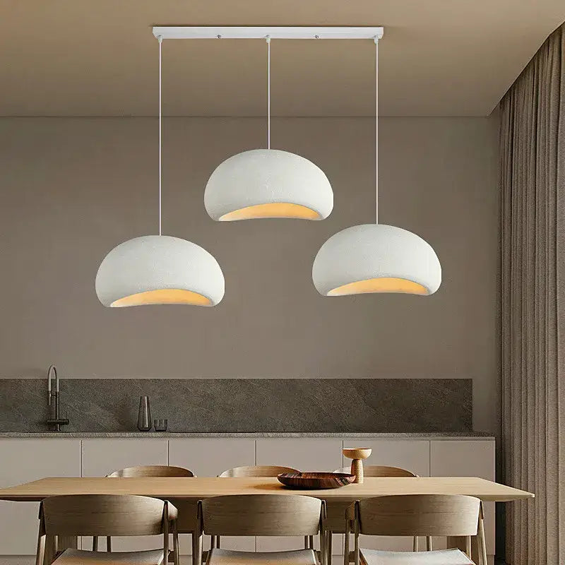Three matte white handmade wabi sabi chandelier pendant lights with rounded domes emit warm light in dining room decorbites style