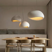 Three off-white handmade wabi sabi pendant lamps with organic cloud shapes hang above a dining table decorbites lamp
