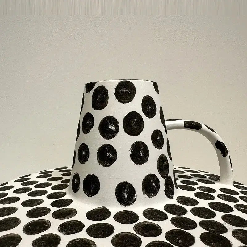White ceramic mug with bold black white dots and matching handle on coordinating dotted decorbites black white surface