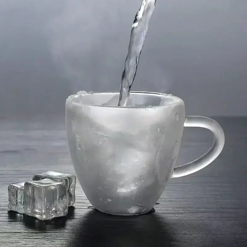 A frosted double wall glass mug with handle filled with steaming hot water surrounded by clear ice cubes