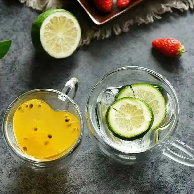 Two clear heart shaped double wall glass mugs one with passionfruit drink and one with water and lime slices